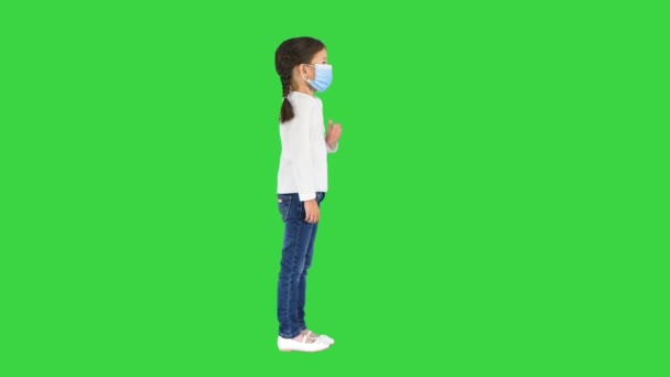 Liten flicka bär skyddande ansiktsmask tar djupa andetag tittar på kameran på en grön skärm, Chroma Key. — Stockvideo