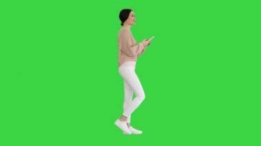 Yeşil Ekran, Chroma Key 'de yürürken cep telefonuyla mesajlaşan güzel genç bir bayan..
