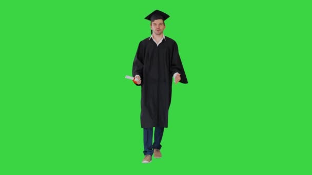 緑の画面、クロマキーの彼の卒業証書と歩いている間、ガウンと迫撃砲の男性卒業生はカメラに話して. — ストック動画