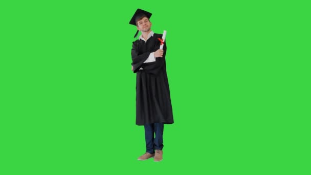 Šťastný muž student v maturitní župan pózování a vzdání se s diplomem na zelené obrazovce, Chroma Key.