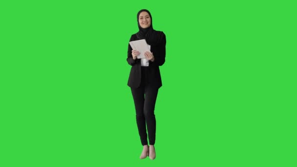 Mujer de negocios árabe en hijab usando tableta mientras camina y sonríe ante la cámara en una pantalla verde, Chroma Key. — Vídeos de Stock