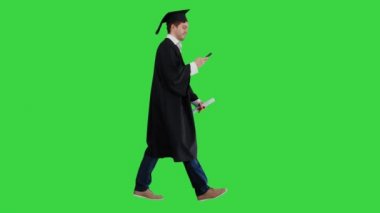 Erkek mezun öğrenci diplomasıyla yürüyor ve yeşil ekranda Chroma Key 'den mesaj yolluyor..