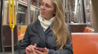 Metroda akıllı telefonunu karıştıran gülümseyen genç bir kız.