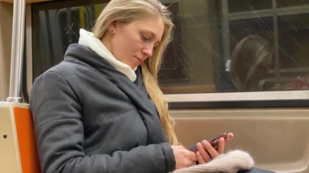 Молодая девушка в зимнем пальто просматривает свой телефон во время поездки в метро — стоковое видео