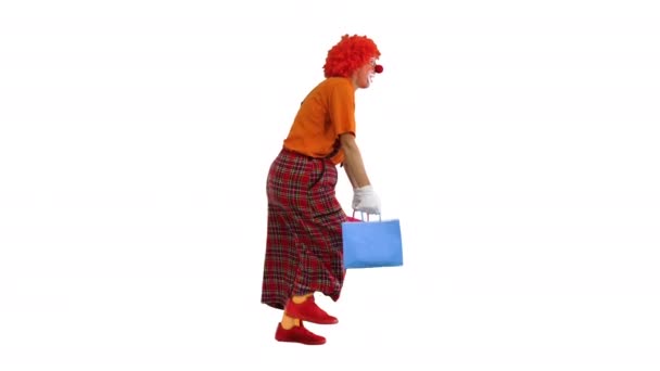 Rolig clown med tunga shoppingväskor promenader på vit bakgrund. — Stockvideo