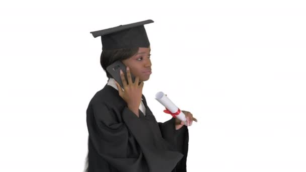Afro-americana estudiante en bata de graduación hablando por teléfono mientras camina sobre fondo blanco. — Vídeos de Stock