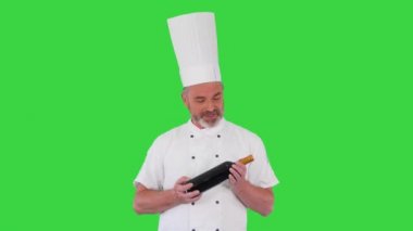 Kıdemli şef elinde bir şişe kırmızı şarap tutuyor ve yeşil ekranda kameraya gülümsüyor, Chroma Key.