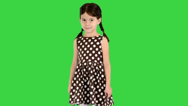 Κοριτσάκι με πουά φόρεμα στέκεται και βάζει τα χέρια στο κεφάλι της σε μια πράσινη οθόνη, Chroma Key. — Αρχείο Βίντεο