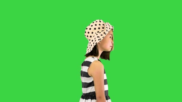 Kis ázsiai lány egy sundress és egy kalap pózol bevásárló táskák a zöld képernyőn, Chroma Key. — Stock videók
