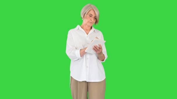 Senior kvinna gör anteckningar i anteckningsblock på en grön skärm, Chroma Key. — Stockvideo