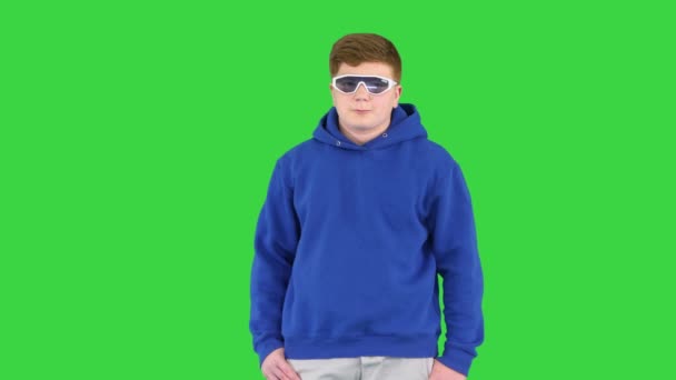 Dreng kid iført afslappet tøj og seje solbriller stående gør noget på en grøn skærm, Chroma Key. – Stock-video