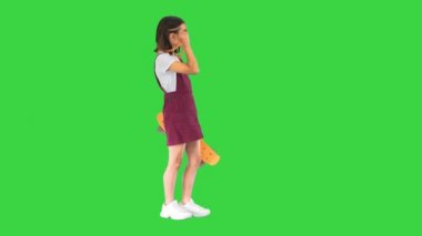 Güneş gözlüklü genç bir kız elinde kaykayıyla yeşil ekranda poz veriyor, Chroma Key..