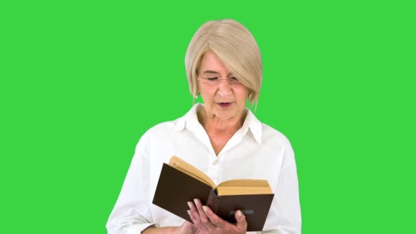Όμορφη ηλικιωμένη γυναίκα που διαβάζει δυνατά από ένα βιβλίο σε μια πράσινη οθόνη, Chroma Key. — Αρχείο Βίντεο