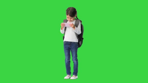 Ragazza della scuola con zaino guardando qualcosa di divertente sul suo telefono rosa e ridendo su uno schermo verde, Chroma Key. — Video Stock