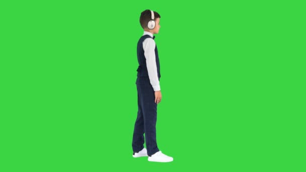 Boy in a bow tie listening to music keeping hands on the headphones on a Green Screen, Chroma Key. — Stock video