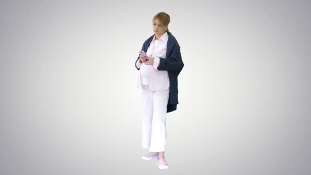 Mooie zwangere vrouw met behulp van haar smartphone aanraken van haar buik staan op gradiënt achtergrond. — Stockvideo