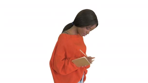 Όμορφη Αφροαμερικανή γυναίκα σε έντονο jumper γράφοντας στο σημειωματάριό της ενώ περπατούσε σε λευκό φόντο. — Αρχείο Βίντεο