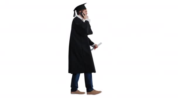 Sorrindo estudante do sexo masculino em roupão de graduação andando e fazendo uma chamada no fundo branco. — Vídeo de Stock