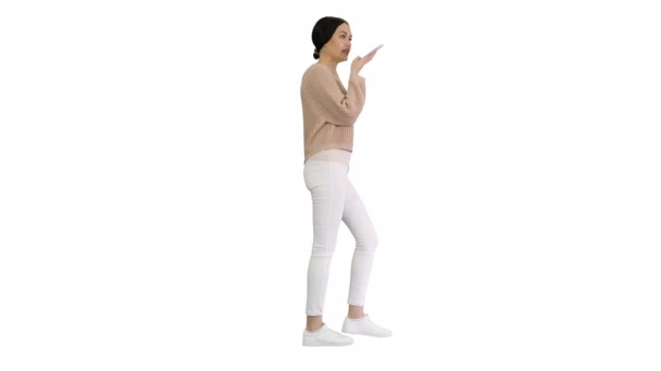 Mujer joven hablando por teléfono sosteniéndolo en su cara mientras camina sobre fondo blanco. — Vídeo de stock