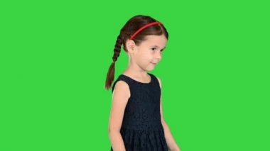 Siyah elbiseli şirin küçük kız ayaklarına bakıyor ve yeşil ekranda gülümsüyor, Chroma Key..
