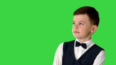 Papyonlu küçük bir çocuk kollarını kavuşturup yeşil ekran Chroma Key 'i düşünerek yukarı bakıyor..