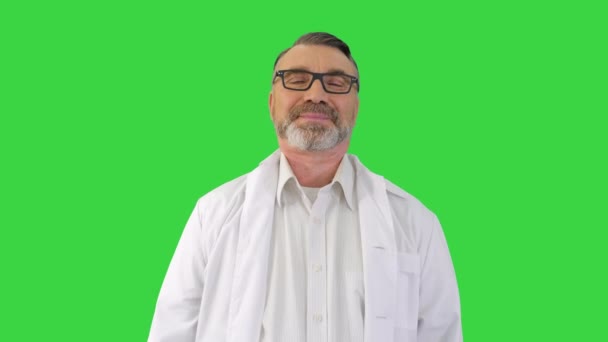 Médico maduro escuchando a alguien detrás de la cámara y sonriendo en una pantalla verde, Chroma Key. — Vídeo de stock