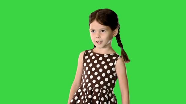 Självsäker liten flicka i polka dot klänning talar om något till kameran och gester på en grön skärm, Chroma Key. — Stockvideo