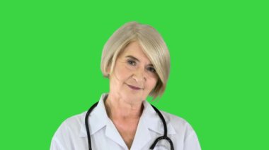 Kıdemli doktor elleri bağlı duruyor ve yeşil ekranda kameraya bakıyor, Chroma Key..
