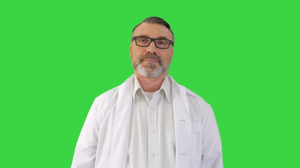 Seriös läkare med glasögon som tittar på kameran och lyssnar på en grön skärm, Chroma Key. — Stockvideo