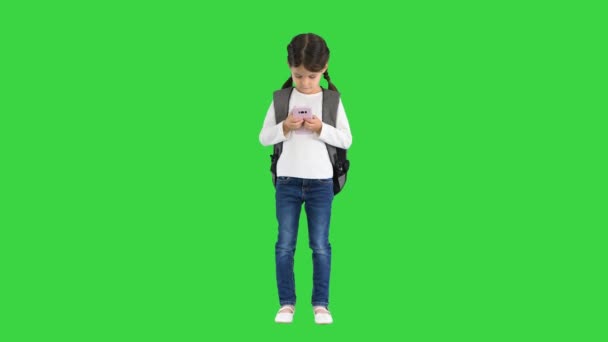 Сконцентрированная школьница с рюкзаком, печатающим на розовом телефоне на зеленом экране, хрома-ключ. — стоковое видео