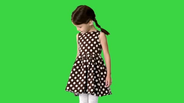 Petite fille en robe à pois regardant autour et vers le bas à ses pieds sur un écran vert, Chroma Key. — Video