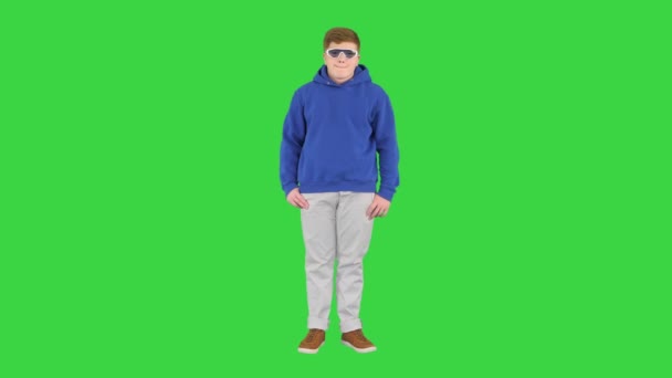 Мальчик в повседневной одежде и классных солнцезащитных очках стоит, ничего не делая на зеленом экране, Chroma Key. — стоковое видео