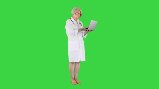 Mature doctor woman standing and working on a laptop on a Green Screen, Chroma Key. — Stock Video