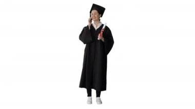 Mezuniyet cüppesi giymiş duygusal bir kız öğrenci telefonda elinde diplomasıyla beyaz arka planda konuşuyor..