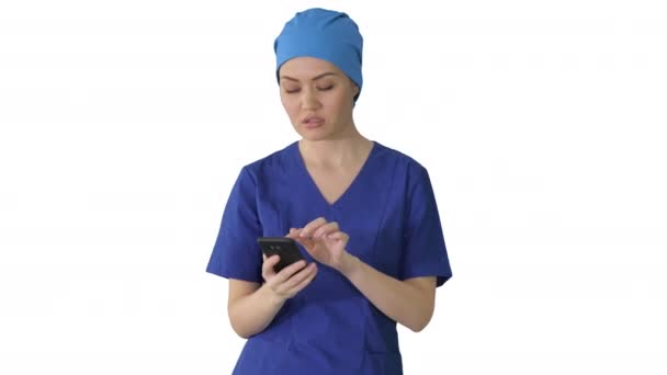 Femme médecin ou infirmière en uniforme bleu en utilisant son téléphone pendant qu'elle marche sur fond blanc. — Video