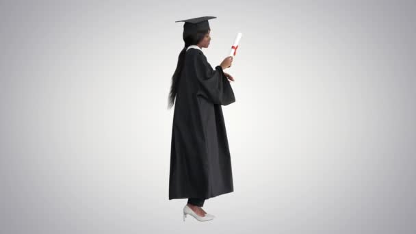 Feliz mujer afroamericana graduada bailando con su diploma en el fondo gradiente. — Vídeo de stock