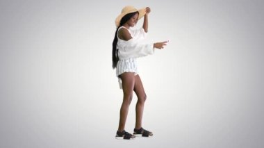 Hasır şapkalı gülümseyen Afro-Amerikan kadın grafiksel arka planda yürürken selfie çekiyor..