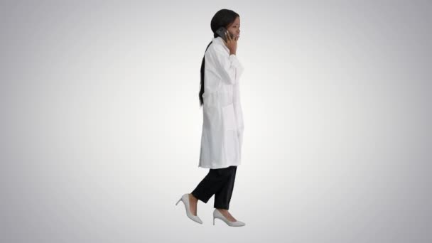 African american female doctor talking on the phone while walking on gradient background. — Stock Video