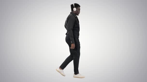 Νεαρός Αφροαμερικάνος που ακούει μουσική με ακουστικά ενώ περπατάει σε βαθμιδωτό φόντο. — Αρχείο Βίντεο