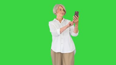 Yeşil Ekran, Chroma Key 'de selfie çekerken gülümseyen ve akıllı telefonunu kullanan yaşlı bir kadın..