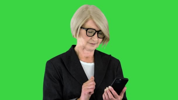 Mooie volwassen vrouw in bril met behulp van een smartphone op een groen scherm, Chroma Key. — Stockvideo