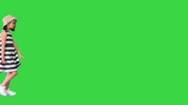 Yazlık kıyafetli küçük bir kız yeşil ekran, Chroma Key 'de kameraya el sallamak için duruyor..
