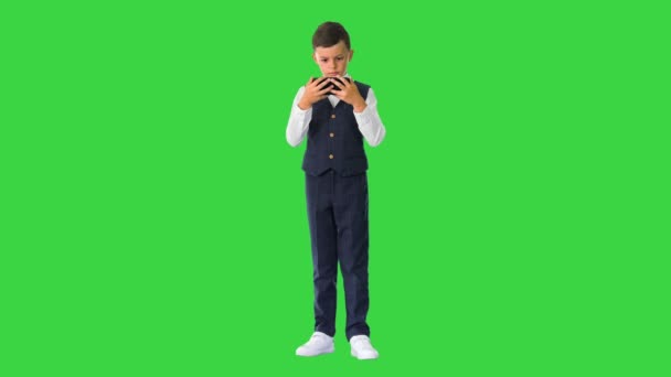 Kleine jongen in vest kijkt iets op zijn telefoon en rondt zijn ogen af in shock op een groen scherm, Chroma Key. — Stockvideo