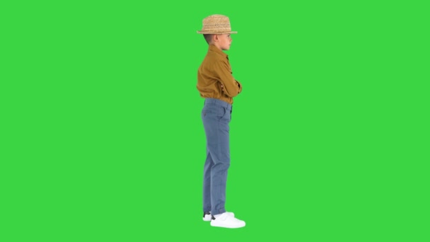 Niño con una camisa y sombrero de paja posando con los brazos cruzados y luego poniendo los brazos en sus caderas en una pantalla verde, Chroma Key. — Vídeo de stock
