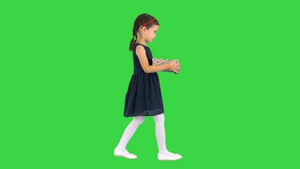 Kleines Mädchen in schwarzem Kleid, das mit einer Geschenkbox in der Hand auf einem Green Screen, Chroma Key, wandelt. — Stockvideo