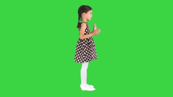 Söt liten flicka i prickig klänning klappar händerna tittar på kameran på en grön skärm, Chroma Key. — Stockvideo