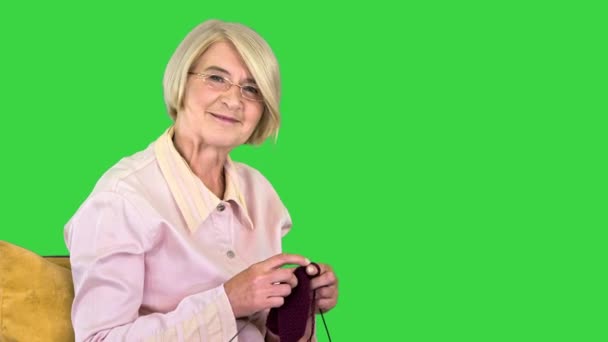 Χαρούμενη ηλικιωμένη γυναίκα πλέκει και ακούει ένα άτομο πίσω από την κάμερα σε μια πράσινη οθόνη, Chroma Key. — Αρχείο Βίντεο