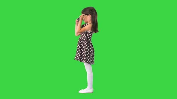 Mörkhårig liten flicka i prickig klänning sätta på svarta solglasögon på en grön skärm, Chroma Key. — Stockvideo
