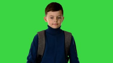 Sırt çantalı bir çocuk yeşil ekran Chroma Key 'de kameraya bakıyor..