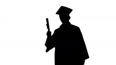 Siluet. Mezuniyet cüppeli mutlu erkek öğrenci diplomasıyla feragat ediyor..